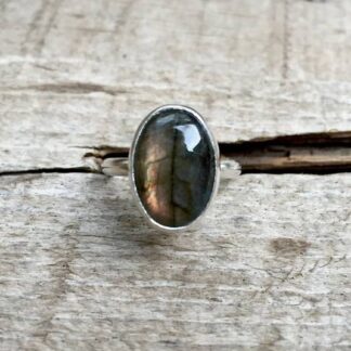 Close-up of an oval labradorite ring on a rustic wooden surface.