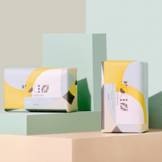 Minimalist yellow and white product packaging displayed on pastel geometric blocks.