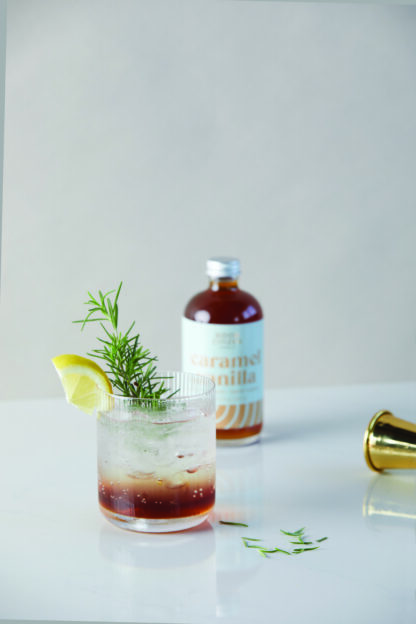 Refreshing cocktail with lemon and rosemary garnish on a white surface.