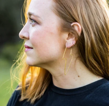 Profile of a woman with light brown hair wearing a black top and hoop earrings.