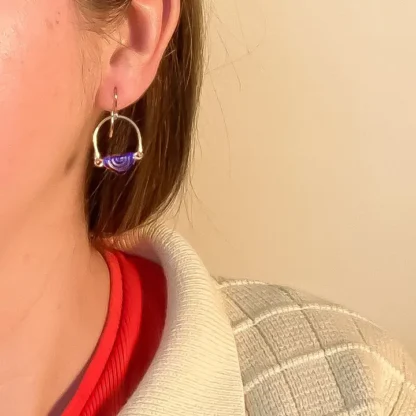 Close-up of a person wearing a purple hoop earring and layered clothing.
