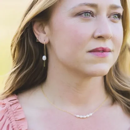 Close-up of a woman wearing pearl earrings and a delicate necklace.