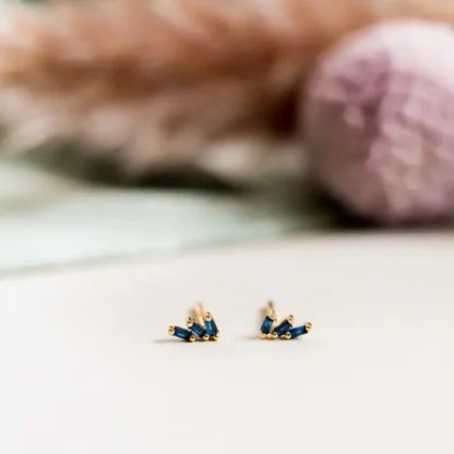 Tiny gold and blue stud earrings on a white surface.