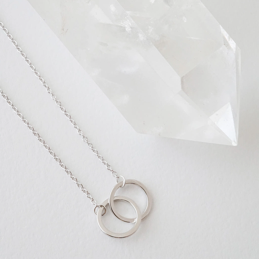 Silver interlocking circle necklace beside crystal